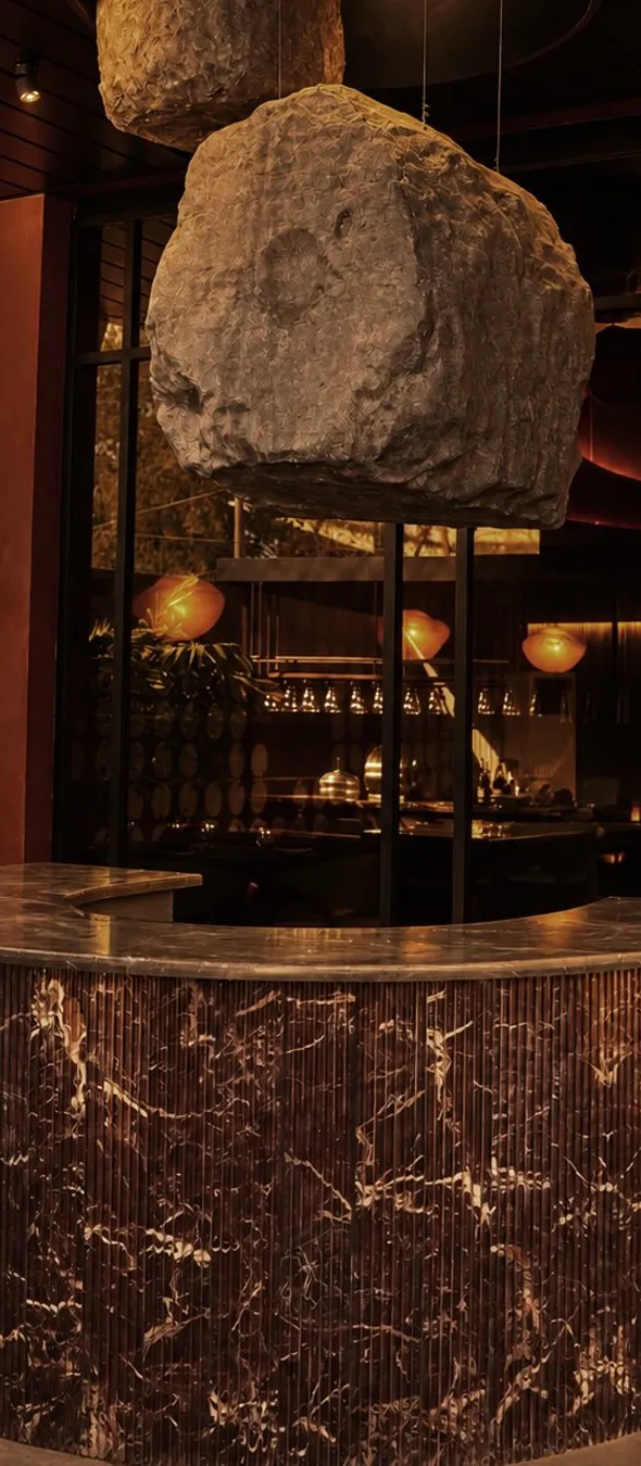 Curved rosso marble bar beneath a suspended boulder