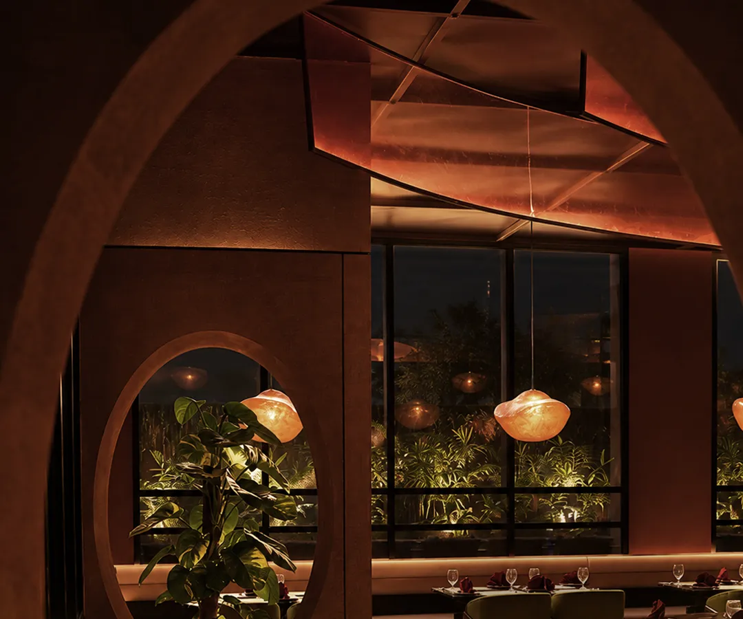 Round window framing a plant beside banquettes and glowing pendant lamps